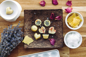 Making of mini wax melts for aroma lamp at home concept. Tools ingredients on table unbleached beeswax, solid coconut oil, essential oil, dried flowers and plastic mold. Above view.