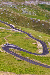 Sharp curves of a freshly paved road wind through grassy and rocky highlands. Construction vehicles...