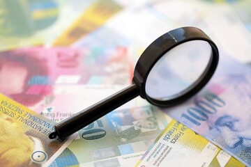 Swiss franc banknotes and magnifying glass. The current francs money bills with loupe lies on table