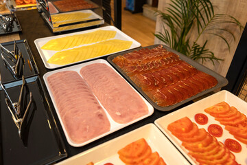Hotel buffet presenting sliced cheese, cooked ham, cured ham, and tomatoes