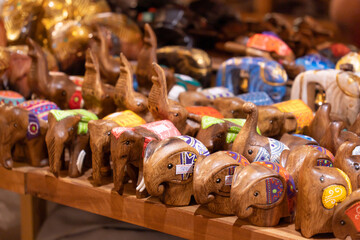 Collection of handcrafted wooden elephant figurines arranged on a display table and selling at a market or craft store.The elephants are carved from wood and decorated with colorful painted patterns.