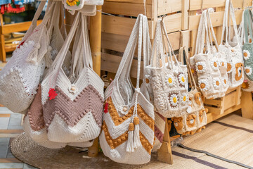 Display of handmade crochet or knitted bags hanging on wooden racks. These bags are typically made from cotton yarn or other natural fibers and are popular for their boho, rustic, or artisanal style.