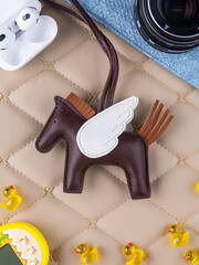 Close-up of a brown leather bag charm in the shape of a cute pegasus with white wings on a table.