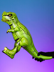 Close-up of a green inflatable Tyrannosaurus dinosaur toy on a purple and blue background