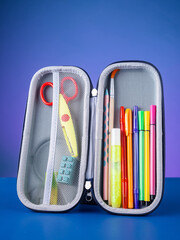 Close-up of a school pencil case with pens, colored pencils, and scissors on a blue background