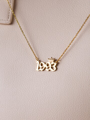 Close-up of a metallic gold pendant in the shape of "1993" on a chain, on a beige leather background
