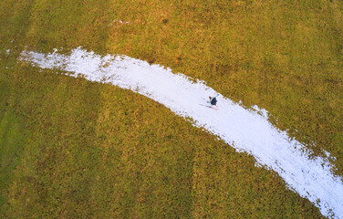 Aerial view of a lone skier gliding down a snow-covered path cutting through golden fields, a stark contrast of winter's touch on autumnal hues, Marktoberdorf, Bavaria, Germany.