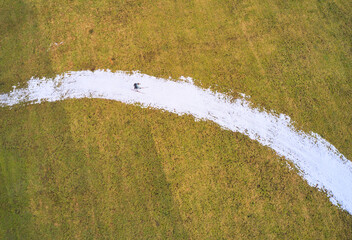 Aerial view of a lone skier glides along a ribbon of snow, contrasting sharply with the golden-green field, Marktoberdorf, Bavaria, Germany.