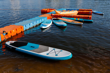 a lot of stand up blue and orange paddle boards on the lake at sunny summer evening with clear blue...