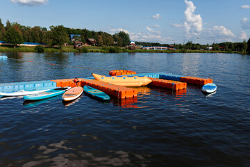 a lot of stand up blue and orange paddle boards on the lake at sunny summer evening with clear blue...