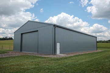 Agricultural barn style steel building surrounded by grass fields for farming, storage, and workshop purposes

