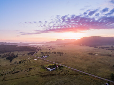 Aerial view of country road through farmland with predawn sunrise glow from behind hills