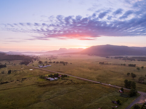Aerial view of country road through farmland with predawn sunrise glow from behind hills