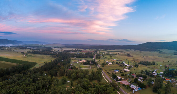 drone view of pink predawn light on cloud over rural village in Hunter Valley hills on horizon