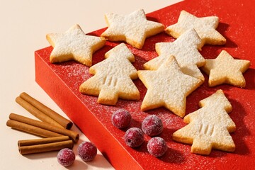 festive assorted star and tree shaped cookies dusted with powdered sugar on red surface with cinnamon sticks and cranberries in holiday setting