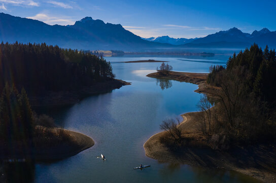 Aerial view of the tranquil lake mirroring the towering Alps, framed by dark forests under the soft morning light, F&Atilde;&frac14;ssen, Bavaria, Germany.