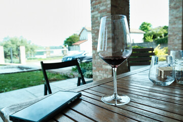 Glass of wine with a cell phone next to it on a table in the greenery of an Italian garden