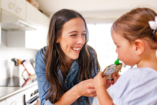Toddler girl standing sipping from food pouch in the kitchen