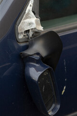 A blue car that has a broken side mirror attached to it, making it difficult to use for safe...