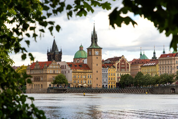 Fototapeta premium Beautiful view of Vltava river,Old Town Water Tower with its clock, the Klementinum, and the dome of church St. Francis of Assisi framed by green leaves. Prague ,Czech Republic 