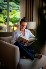 Smiling middle aged woman relaxing at home and reading a book