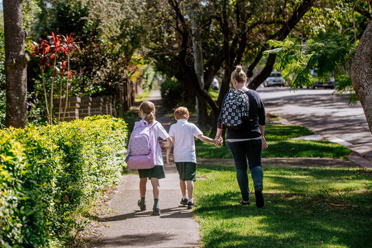 Back profile of mother holding hands with her children on walking path