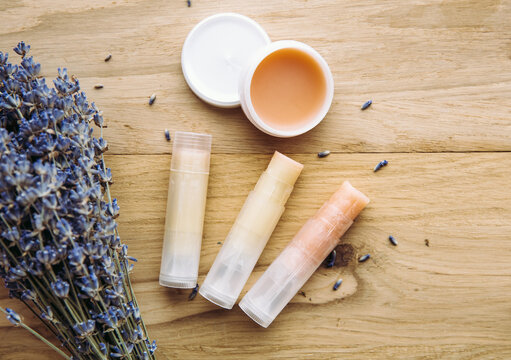 Homemade natural organic ingredients hygienic lipstick. Handmade lip balm and lipstick inside container on natural wooden background and lavender bouquet for decoration.