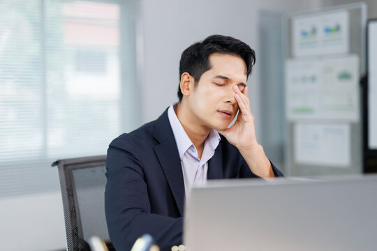 Asian businessman having headache and massaging his head at office desk, tired after long work on laptop computer - Powered by Adobe