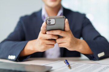 Businessman sitting at a desk in an office, holding a mobile phone and reading the latest news while staying focused on work tasks