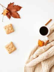 Warm beverages and sweater with autumn leaves, cinnamon sticks, and crackers arranged on a white surface for cozy lifestyle