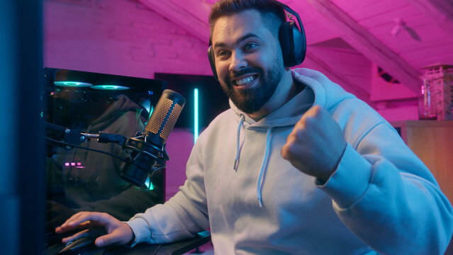 Excited winner champion Caucasian guy male gamer streamer man winning luck achievement victory internet win talking microphone play online game addict in headphones gaming streaming in neon dark room