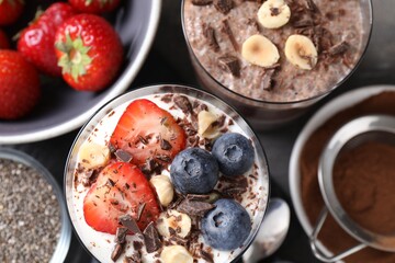 Delicious chocolate puddings with chia seeds, nuts and berries in glasses on grey table, flat lay