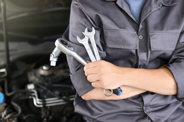 Auto parts. Professional mechanic with different wrenches near open hood of car indoors, closeup....
