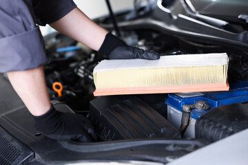 Auto part. Professional mechanic with air filter near open hood of car indoors, closeup