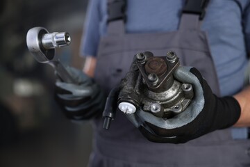 Auto part. Professional mechanic with hydraulic pump and socket wrench indoors, closeup