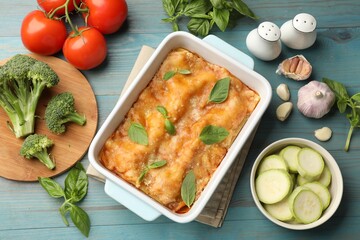 Tasty vegetarian lasagna in baking dish and ingredients on blue wooden table, flat lay
