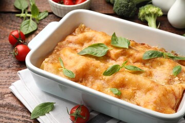 Tasty vegetarian lasagna in baking dish and ingredients on wooden table, closeup