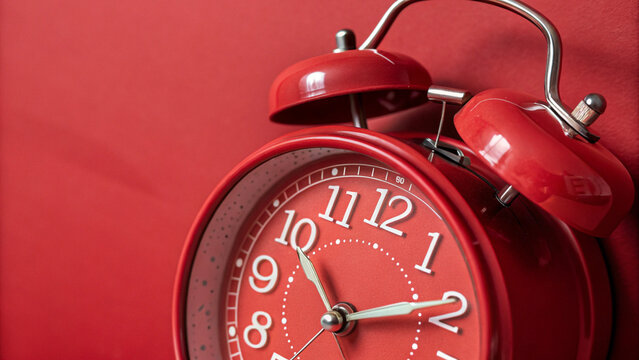 Close-up shot of a classic red alarm clock against a matching red background. The minimalist monochrome composition emphasizes time, urgency, and punctuality. Ideal for concepts related to deadlines, 