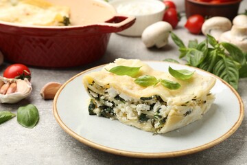 Piece of tasty vegetarian lasagna and ingredients on grey table, closeup