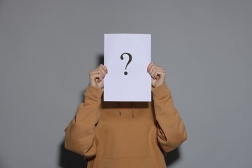 Anonymity. Woman hiding behind paper sheet with question mark on light grey background