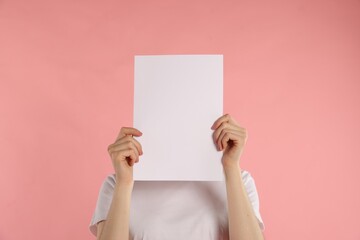 Anonymity. Woman hiding behind blank paper sheet on pink background