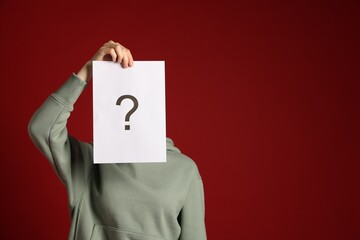 Anonymity. Woman hiding behind paper sheet with question mark on dark red background, space for text