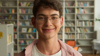 Close up portrait happy Caucasian male student man guy teenager smiling carefree looking at camera in library books store education studying learning in school college teen wearing glasses headshot