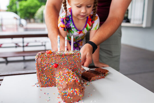 Three year old girl cutting birthday cake shaped like a camera with hundreds and thousands
