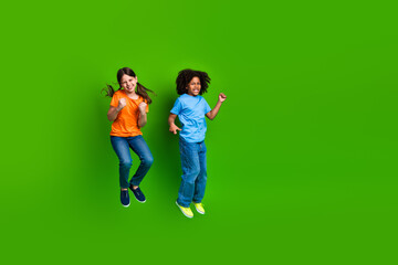 Two happy children joyfully jumping against a vibrant green background, celebrating playtime and friendship together