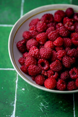 Plate of freshly picked red raspberries on green tile background. Concept of vibrant colors, summer, harvest, healthy organic food.
