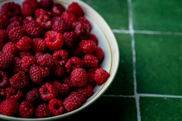 Plate of freshly picked red raspberries on green tile background. Concept of vibrant colors, summer, harvest, healthy organic food.