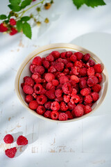 Plate of freshly picked raspberries on white wooden background. Concept of harvest, healthy organic food, summer berries.