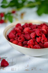 Plate of freshly picked raspberries on white wooden background. Concept of harvest, healthy organic food, summer berries.