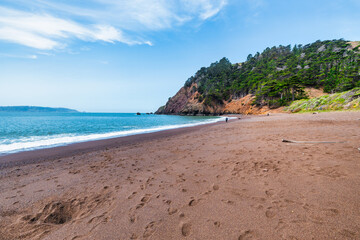 Kirby Cove Beach in California with red sand, blue ocean waves, and dramatic cliffs covered in pine trees. A hidden gem near San Francisco, perfect for nature, travel, and coastal exploration themes